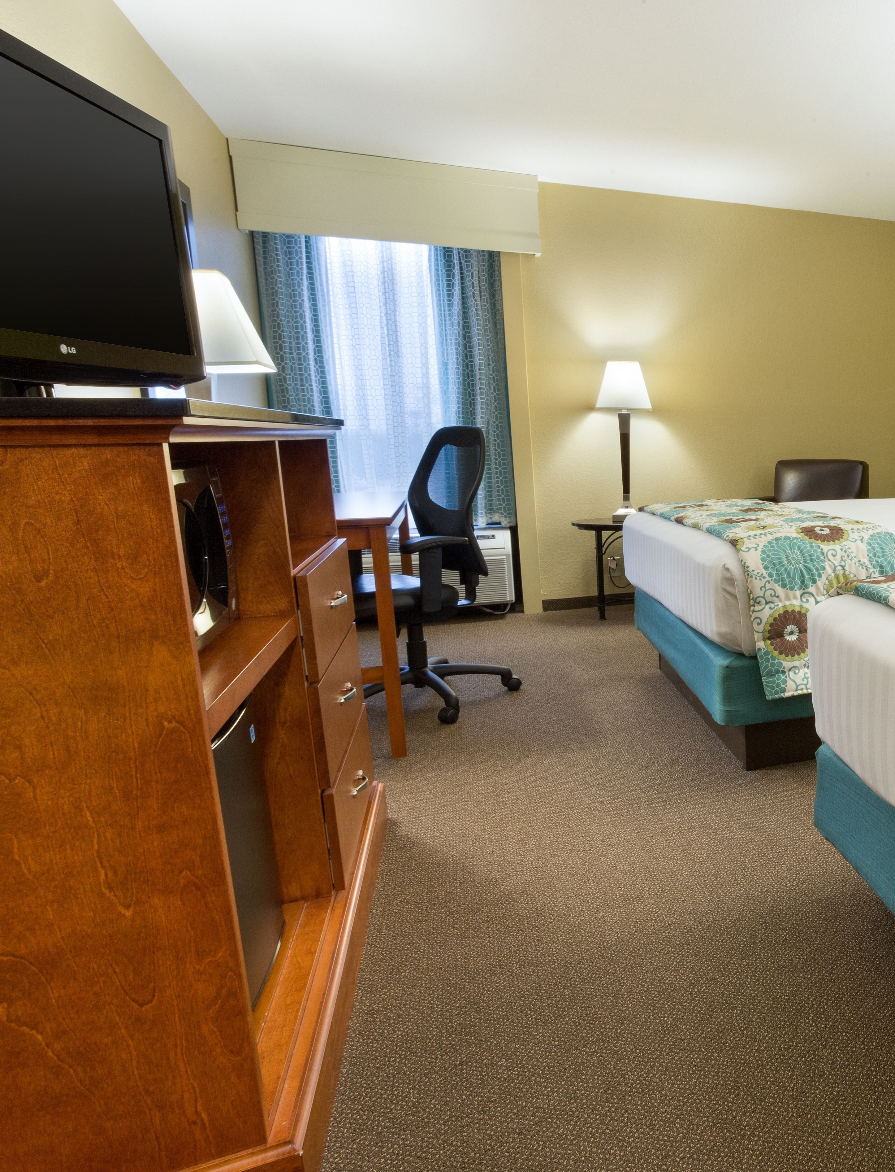 A hotel room with a bed, a desk with a chair, a television, and a lamp.