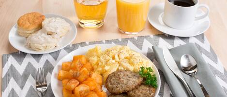 A breakfast plate with biscuits, scrambled eggs, hash browns, and sausage links, accompanied by two glasses of orange juice and a cup of coffee.