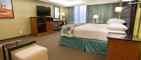 A hotel room with a bed, a desk with a television, a chair, a small table, and a mirror.