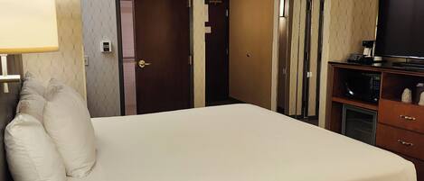 A hotel room with a large bed, a desk with a lamp, a television, and a microwave.