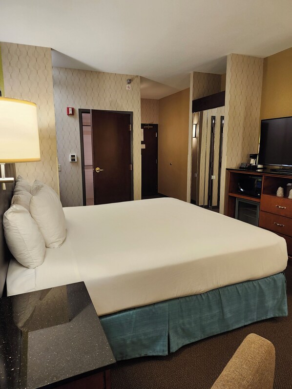 Una habitación de hotel con una cama grande, un escritorio con lámpara, televisor y microondas.