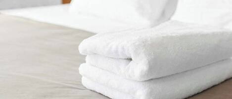 Una toalla blanca doblada cuidadosamente sobre una cama con sábana en tonos claros.