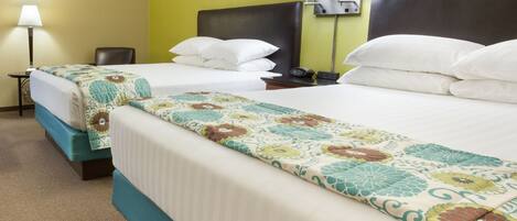 A hotel room with two beds, a nightstand with a lamp, and a wall with framed pictures.