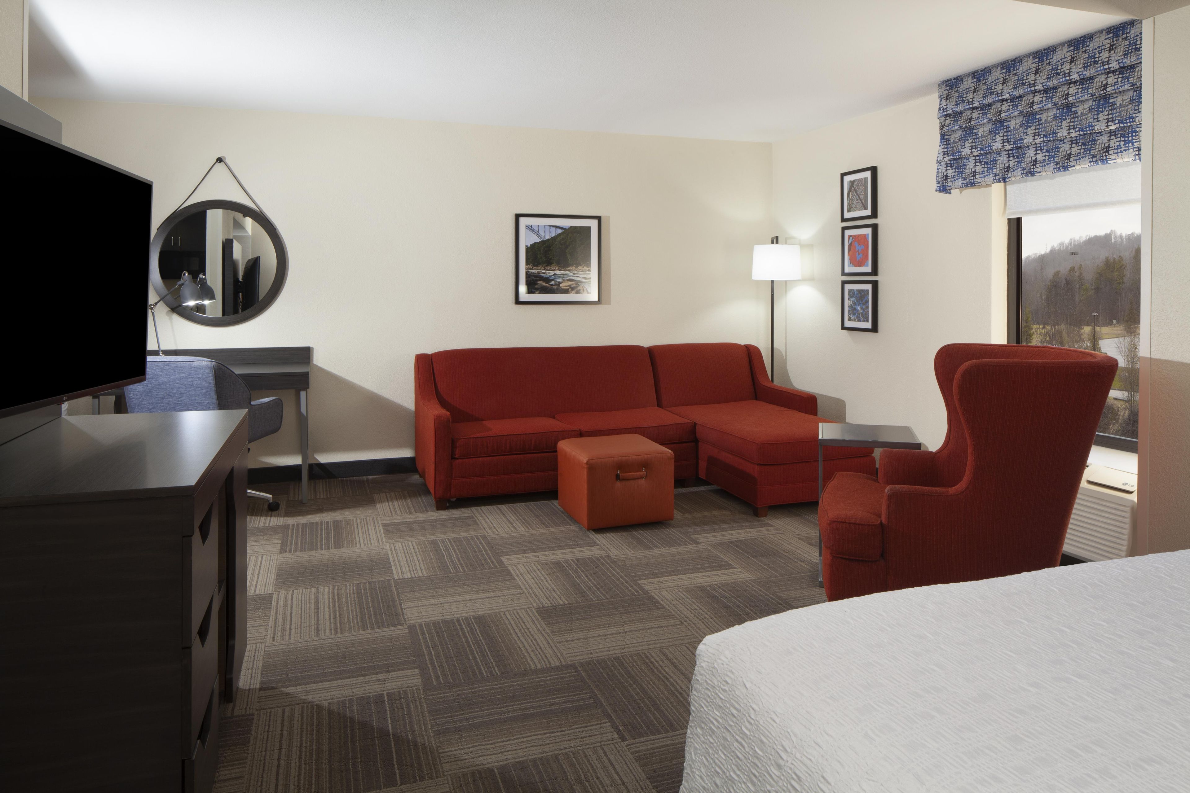 A hotel room with a sofa, a chair, a desk, a television, and a window with a view.