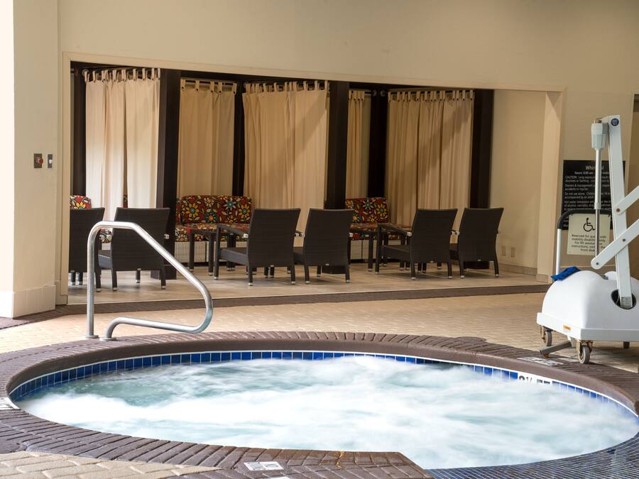 A hot tub area with a pool table and chairs, a wheelchair-accessible lift, and a sign with safety instructions.