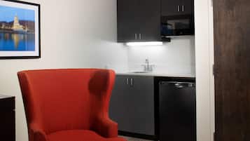 A compact kitchen with dark cabinets, a sink, and a dishwasher. A red chair is positioned in front of the kitchen.