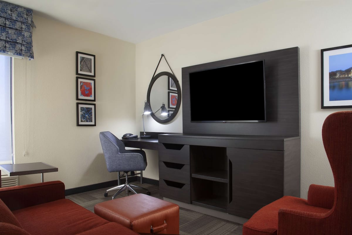 Ein Hotelzimmer mit Flachbildfernseher, Schreibtisch mit Stuhl, rotem Sofa, rotem Sessel und Wandspiegel.