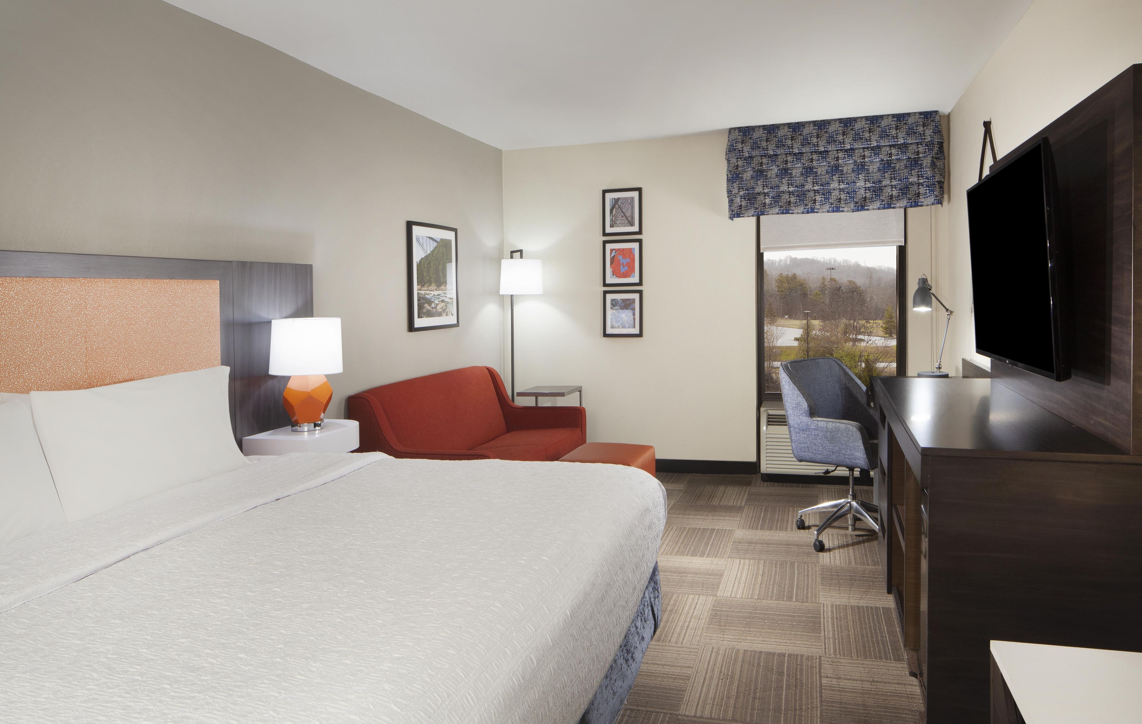 A hotel room with a bed, a desk, a chair, a TV, and a window with a view.