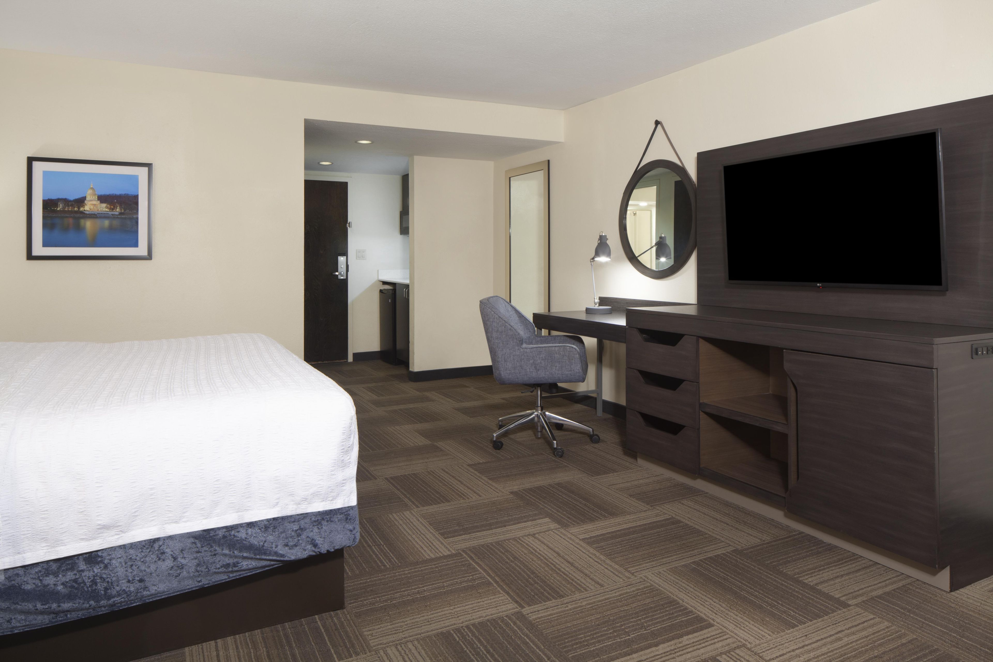 A hotel room with a bed, a desk, a chair, a television, and a framed picture on the wall.