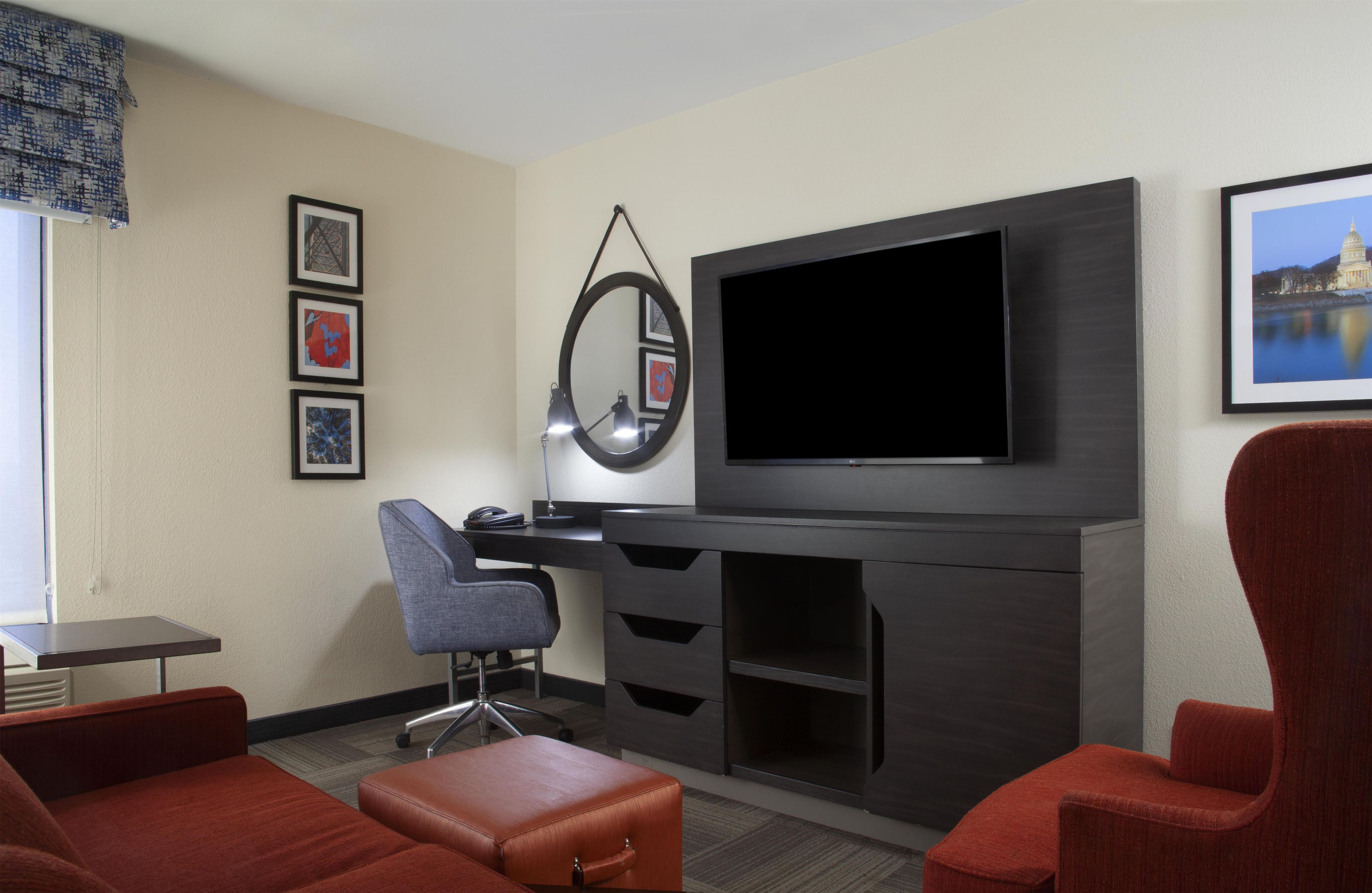 A hotel room with a flat-screen TV, a desk, a chair, a couch, and a large mirror.