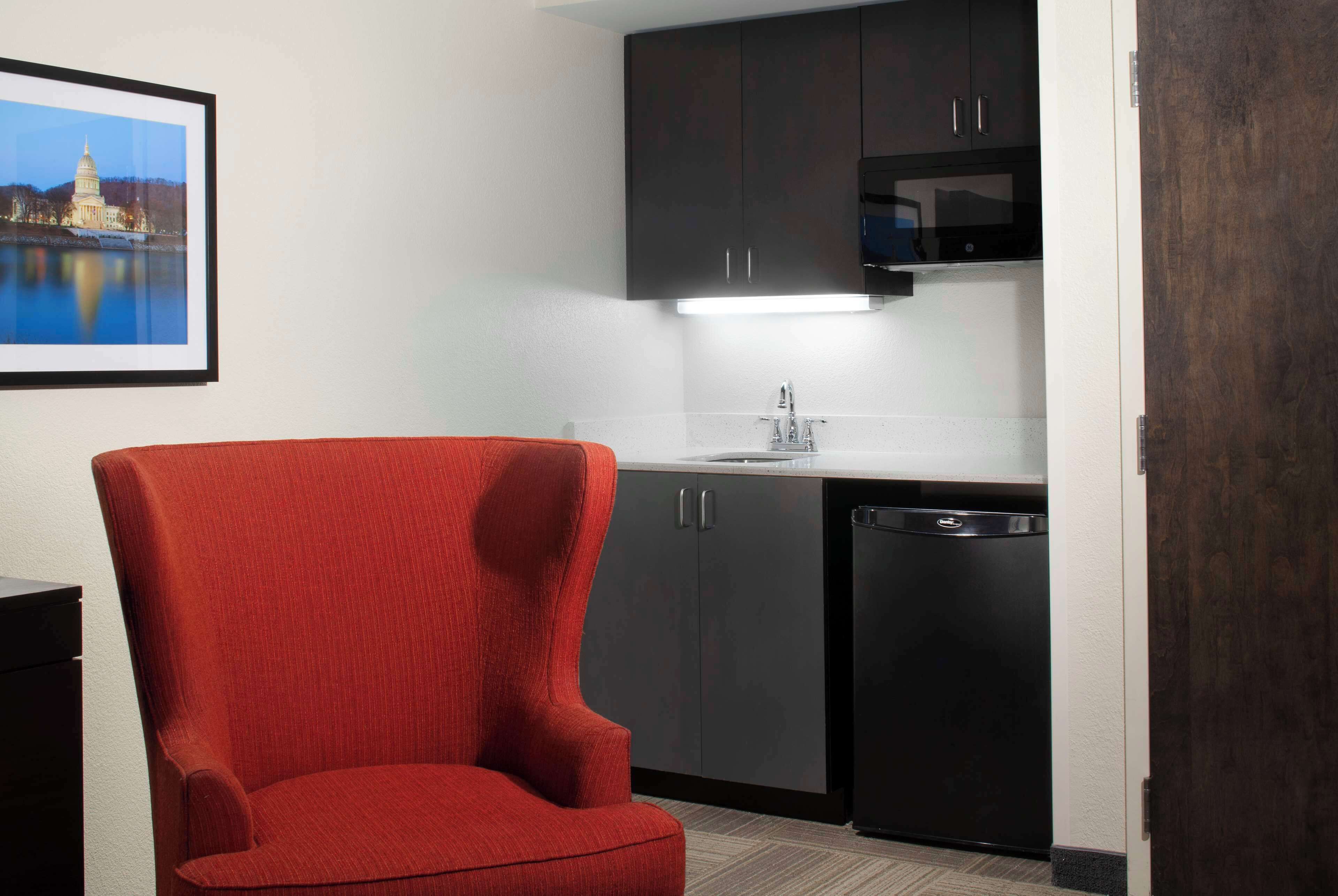 A compact kitchen with dark cabinets, a black dishwasher, and a red chair.