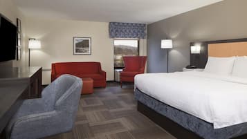 A hotel room with a bed, a desk, a chair, a sofa, and a television.