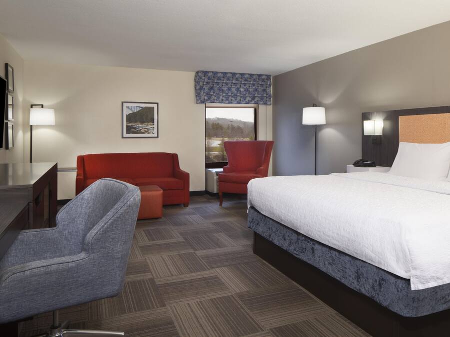A hotel room with a bed, a desk, a chair, a sofa, and a television.