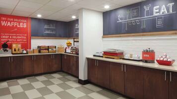 A kitchen area with waffle-making equipment, a waffle station, and a counter with various food items.