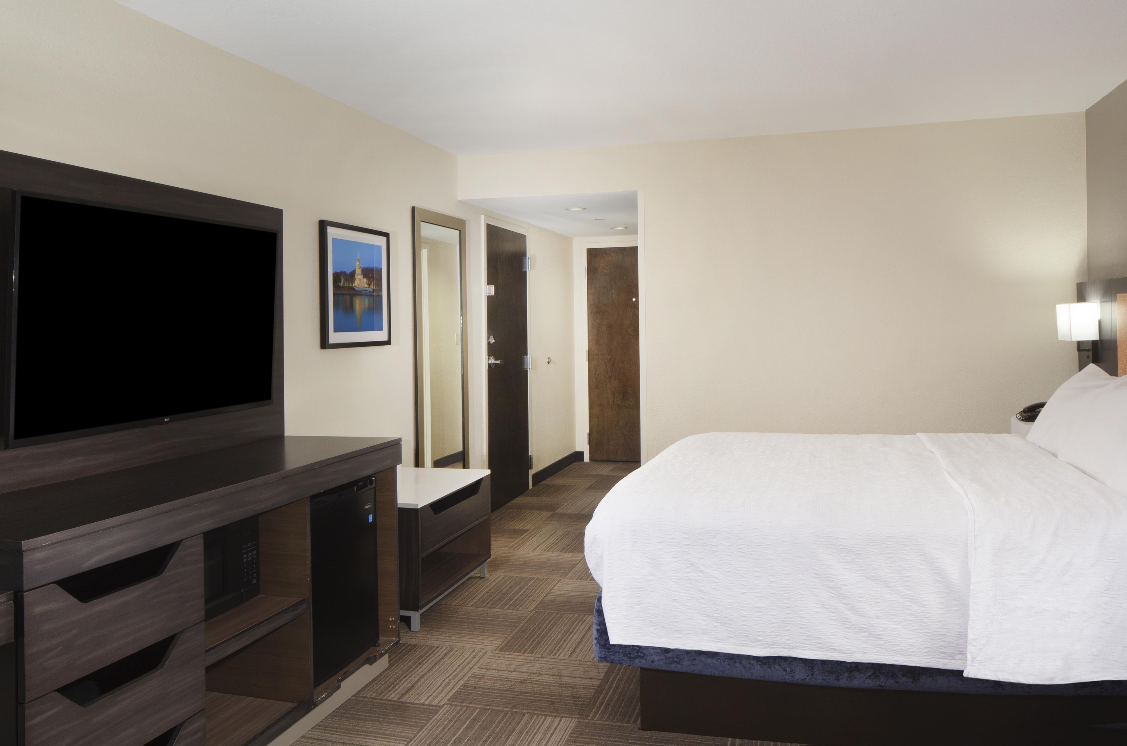 A hotel room with a bed, a flat-screen TV, a dresser, and a door leading to another room.