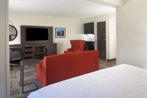 Habitación de hotel con cama, escritorio, televisor de pantalla plana, sillón rojo y una pequeña mesa.