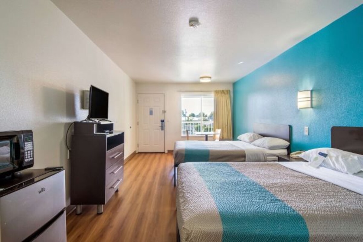 A hotel room with two beds, a desk with a TV, and a view of the city.