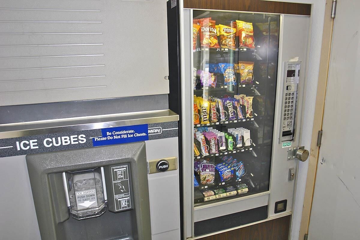 A vending machine with a sign for ice cubes and a variety of snacks.