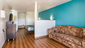 Un espace de vie compact doté d’un plancher en bois, d’un canapé à motifs floraux, d’une petite kitchenette et d’un mur d’accent bleu.