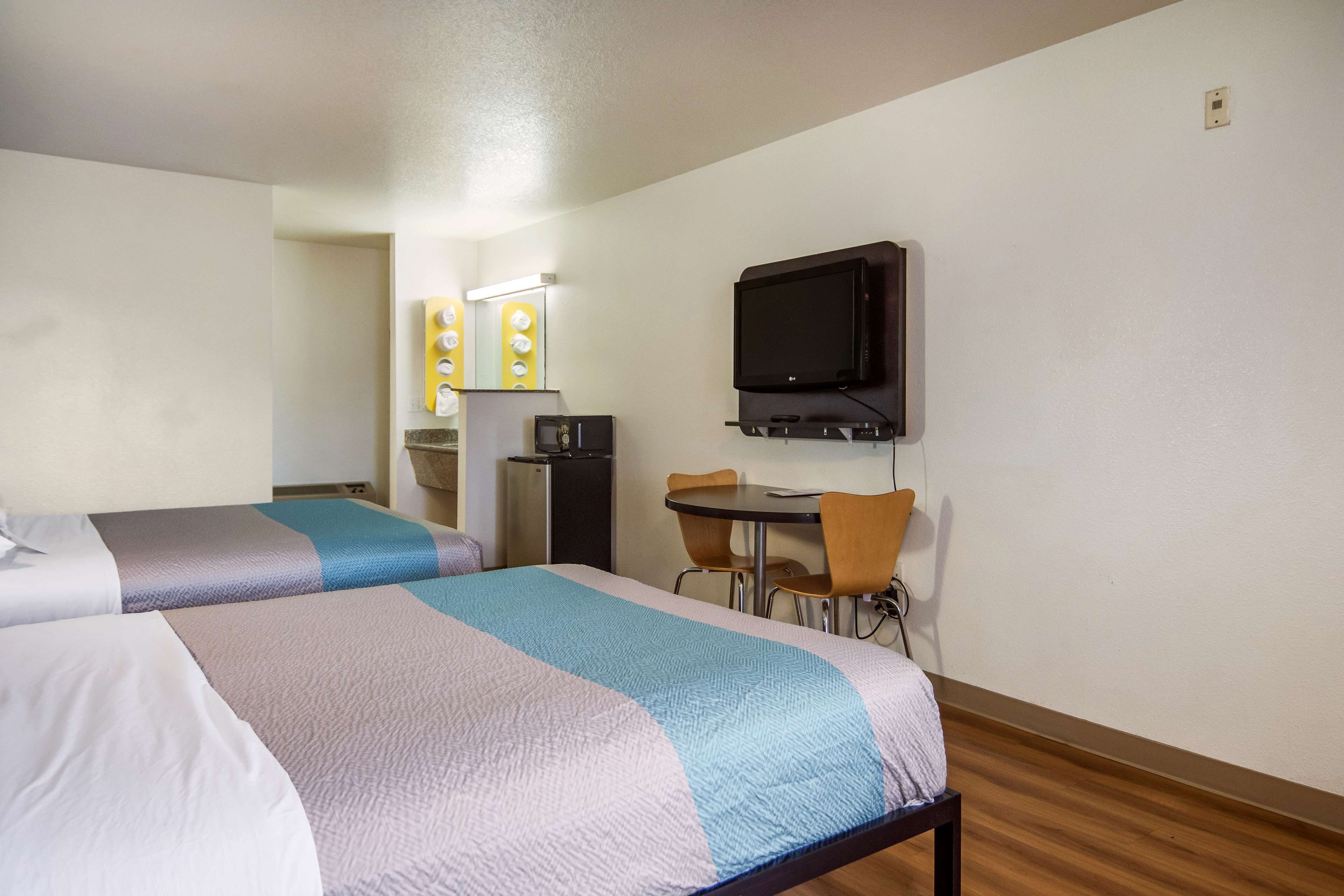 A hotel room with two beds, a desk, a television, and a refrigerator.