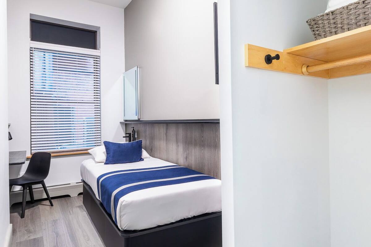 Et moderne hotelværelse med seng, skrivebord og vindue med persienner.