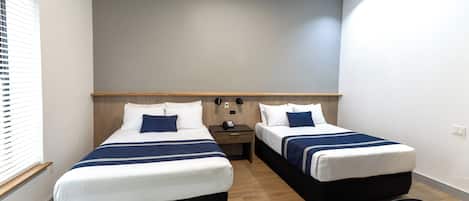 Habitación de hotel con dos camas, un cabecero de madera, una mesita de noche con teléfono y un escritorio con silla.