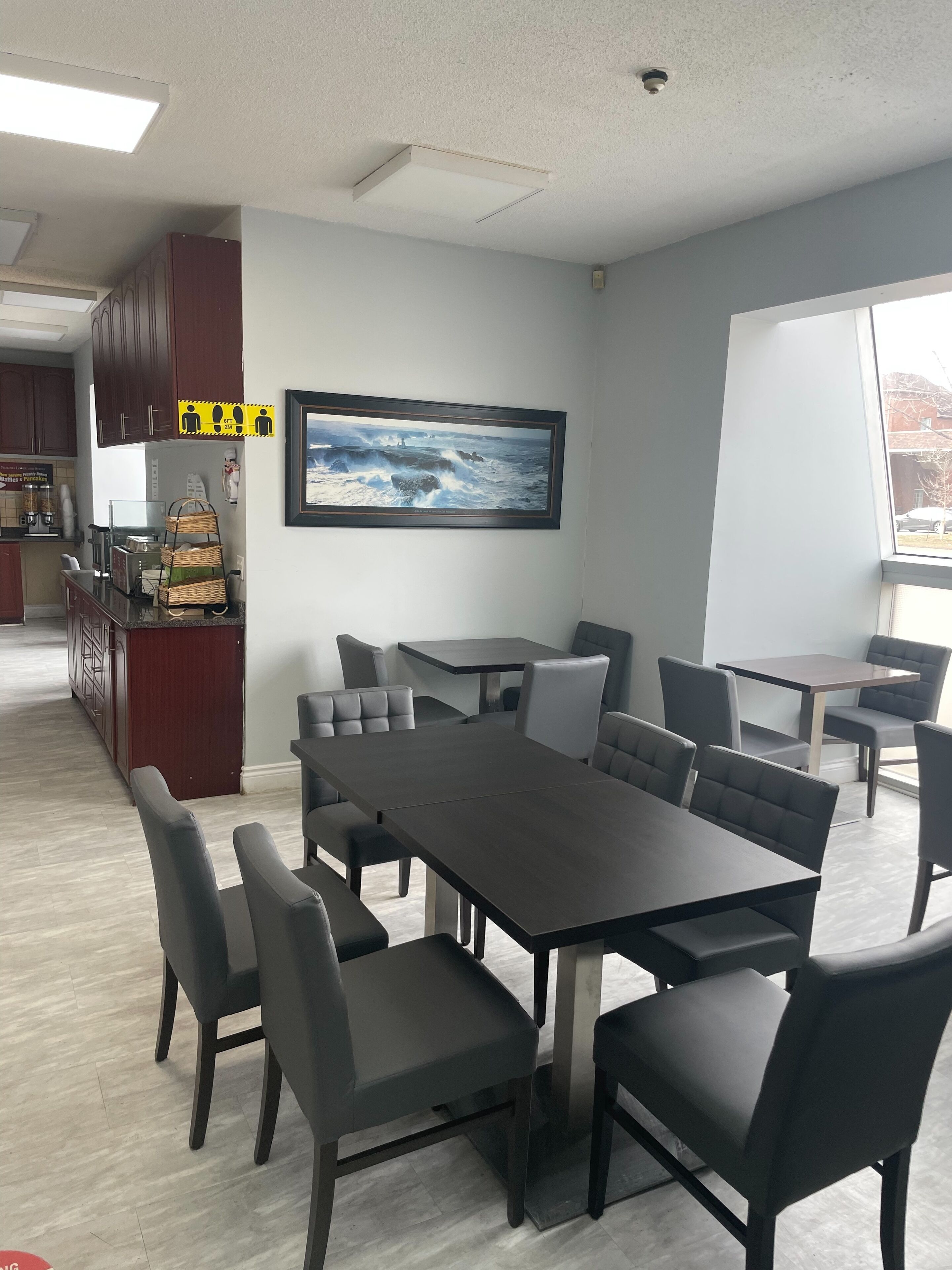 A conference room with a long table and chairs, a kitchen area with cabinets and appliances, and a large window with a view of buildings.