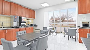 A modern kitchen with wooden cabinets, a refrigerator, a microwave, and a dining area with a table and chairs.
