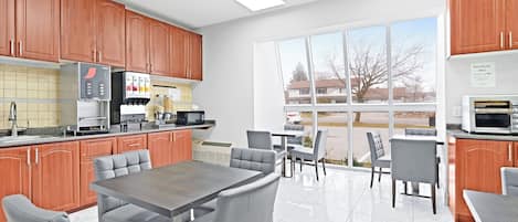 A modern kitchen with wooden cabinets, a refrigerator, a microwave, and a dining area with a table and chairs.
