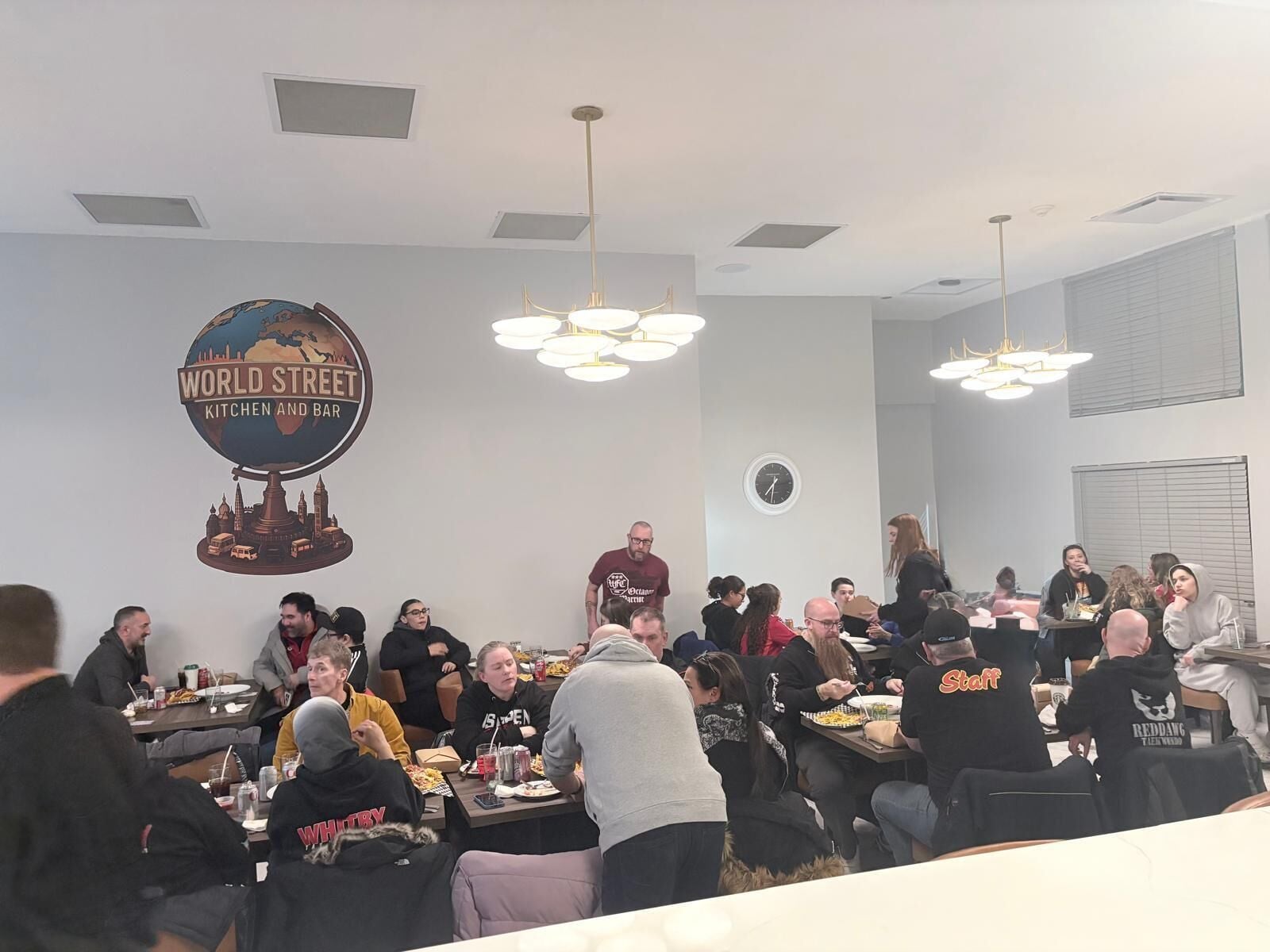 A group of people seated at tables in a room with a 'World Street Kitchen and Bar' sign on the wall.