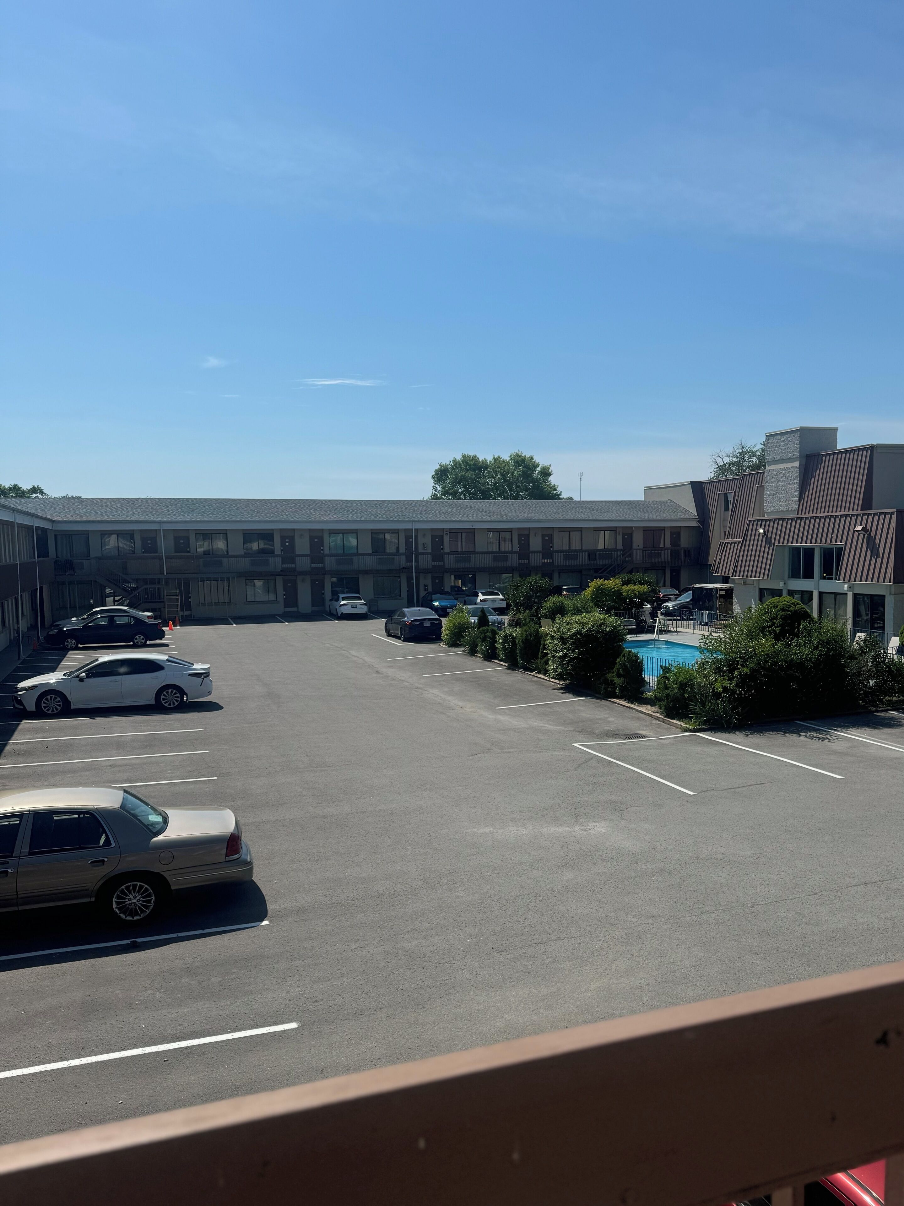 A parking lot with several cars, a building with a modern design, and a swimming pool area.