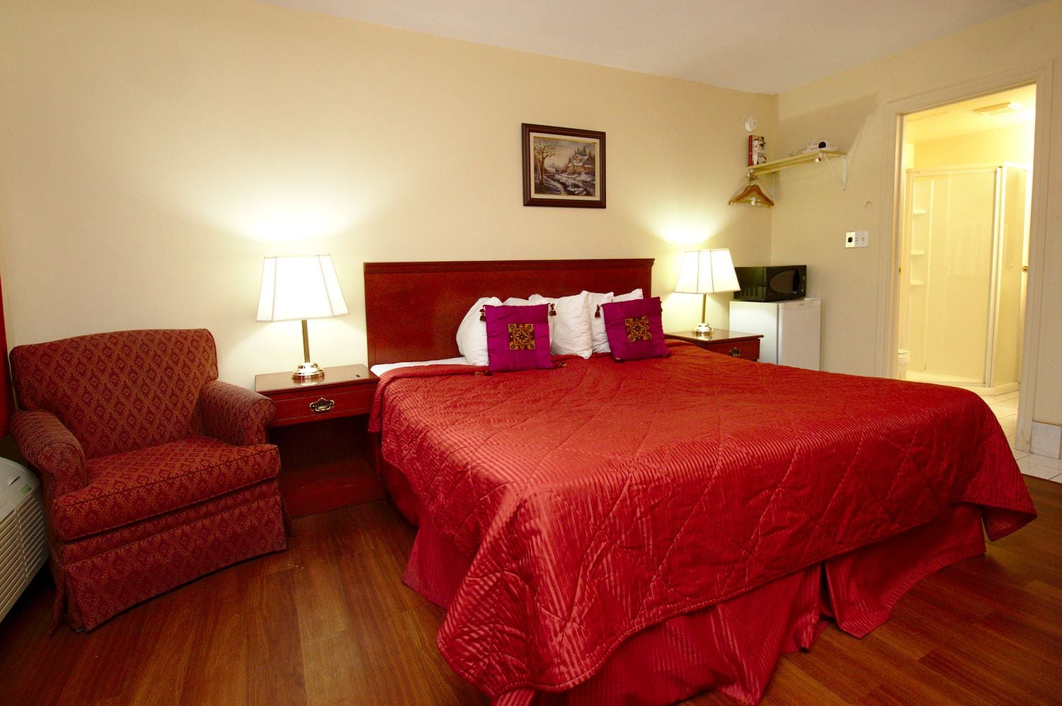 Quarto de hotel com uma cama grande, duas mesas de cabeceira, uma cadeira e um quadro na parede.