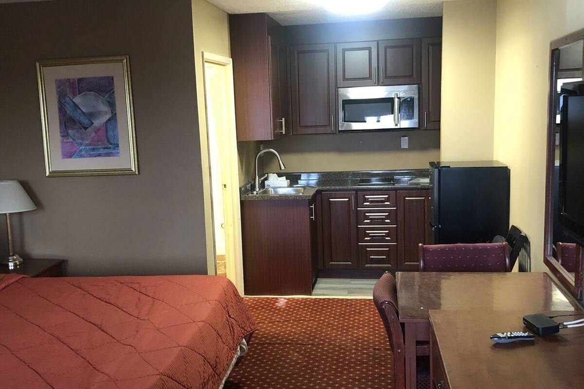A hotel room with a bed, a desk with a chair, a kitchenette with a microwave, and a television.