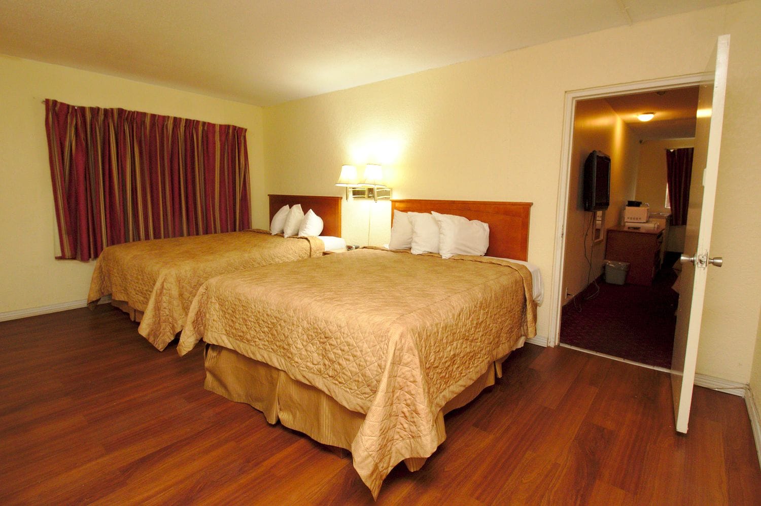 Een hotelkamer met twee bedden, een houten vloer, een nachtkastje met een lamp en een deur naar de badkamer.