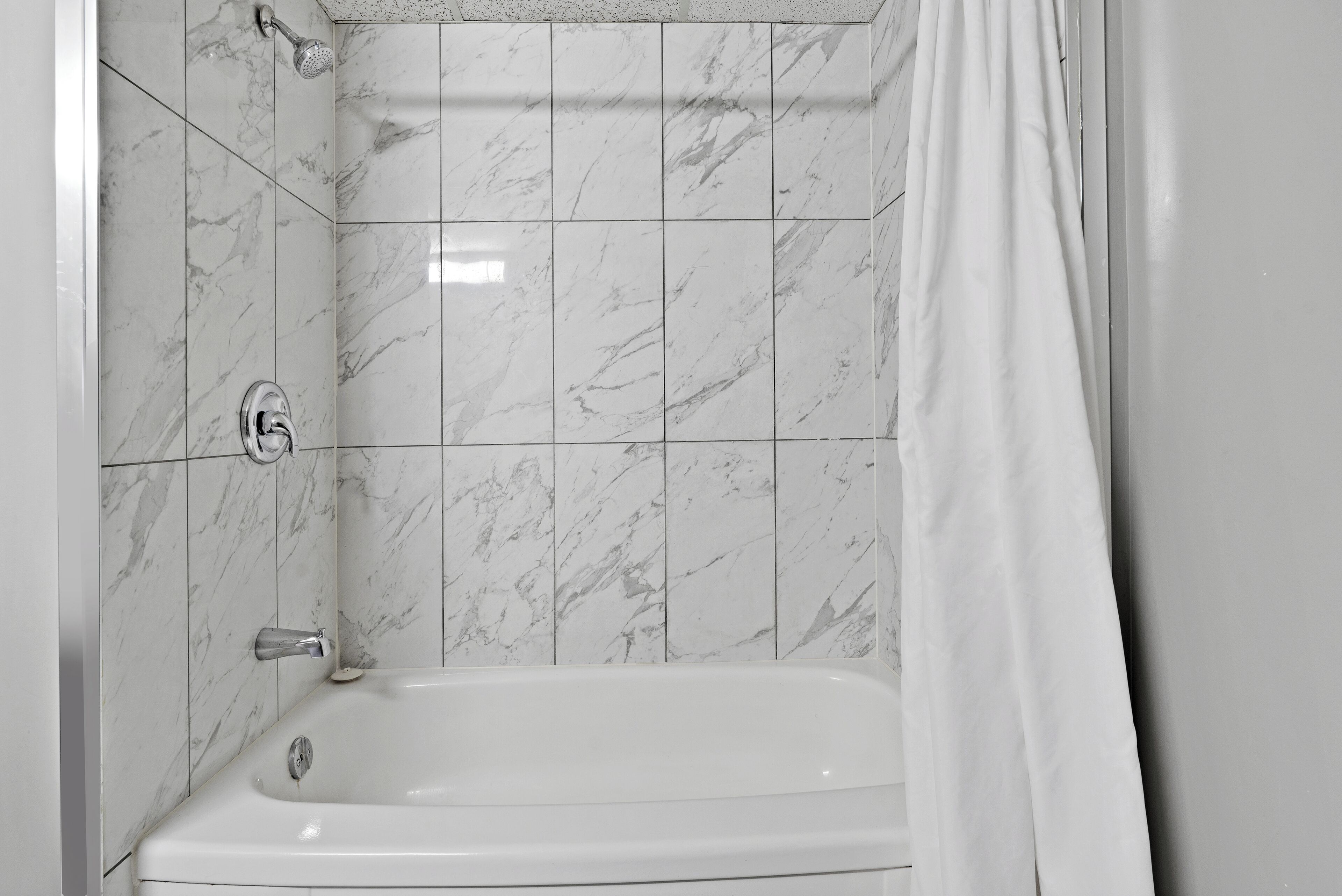 A bathroom with a white bathtub, marble tiles, and a showerhead.
