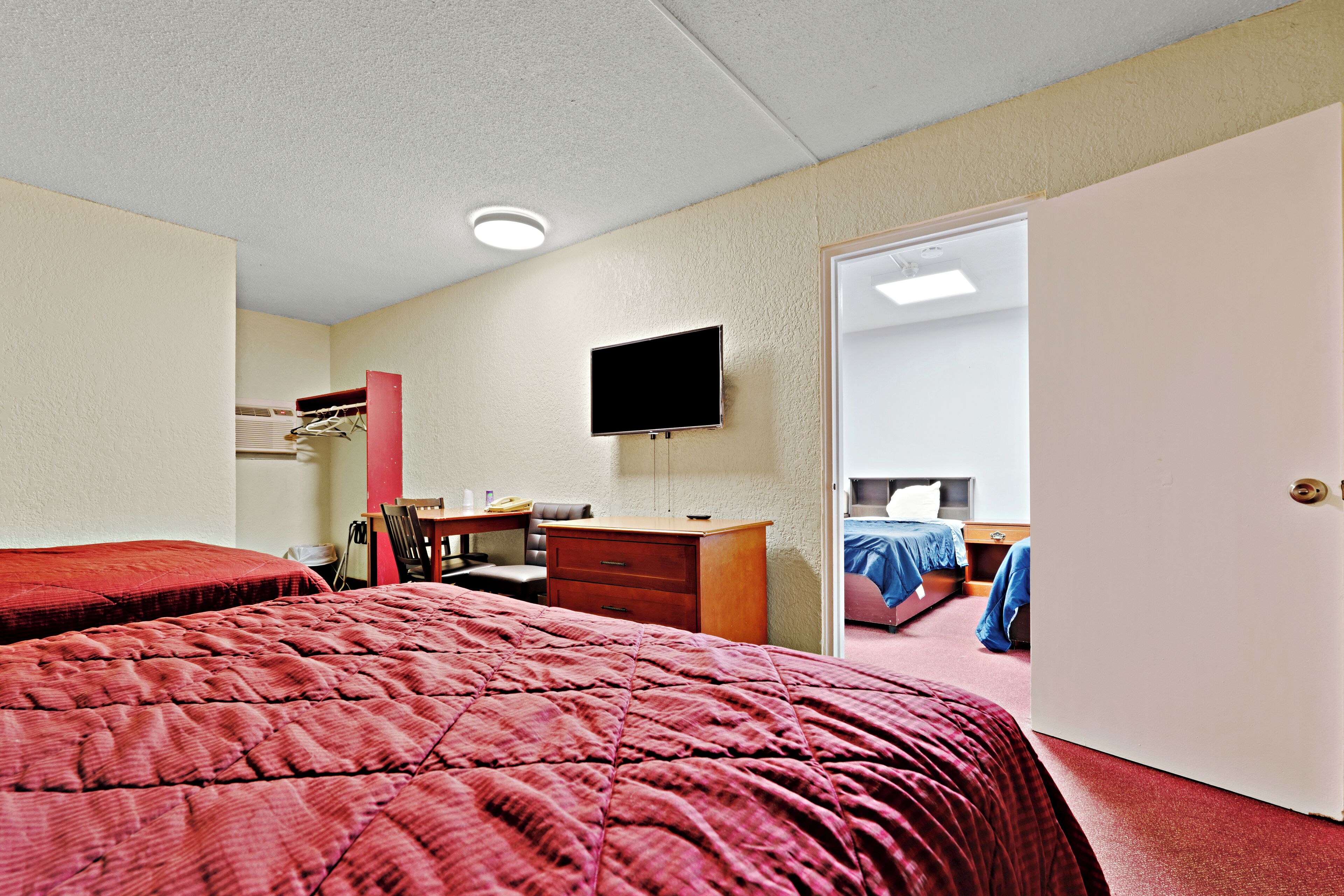 A hotel room with two beds, a desk, a chair, a television, and a door leading to another room.