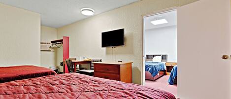 A hotel room with two beds, a desk, a chair, a television, and a door leading to another room.