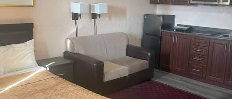 A hotel room with a bed, a sofa, a kitchenette with a microwave, and a painting on the wall.
