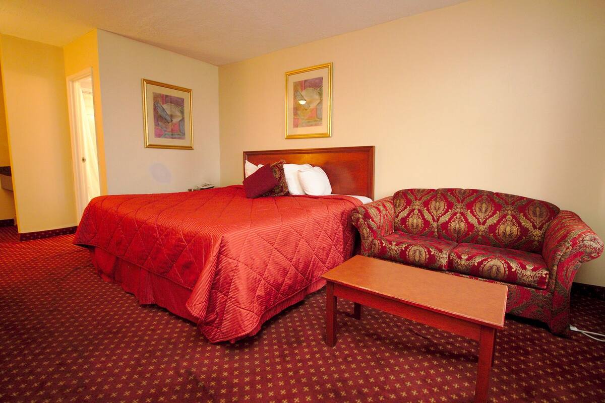 A hotel room with a bed, a sofa, and a small table. There are two framed pictures on the wall.