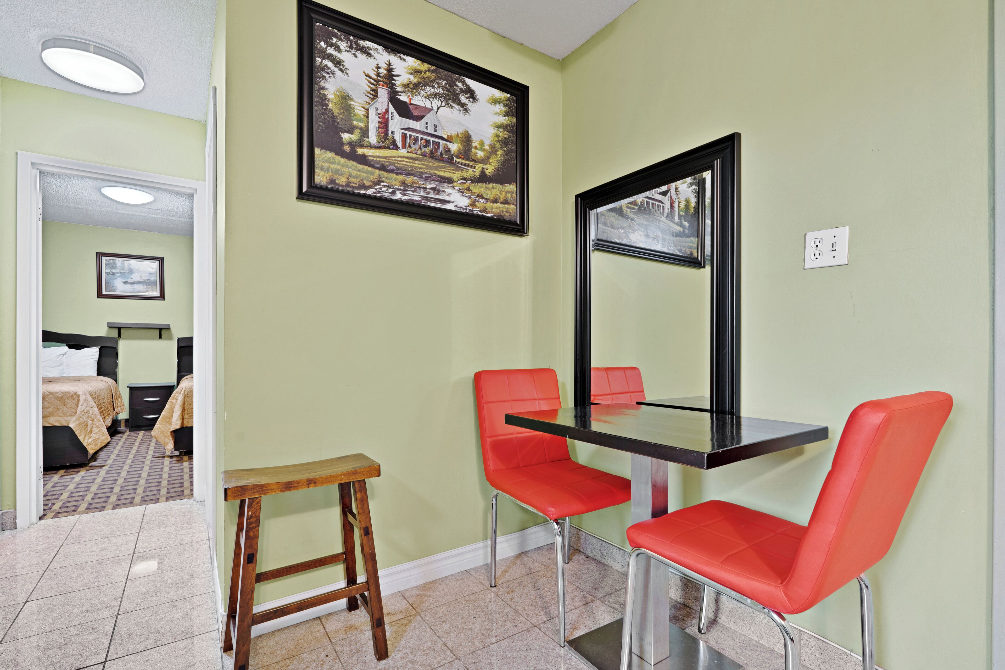 Une pièce comprenant une table à manger, deux chaises rouges, un tabouret en bois et un tableau encadré accroché au mur.