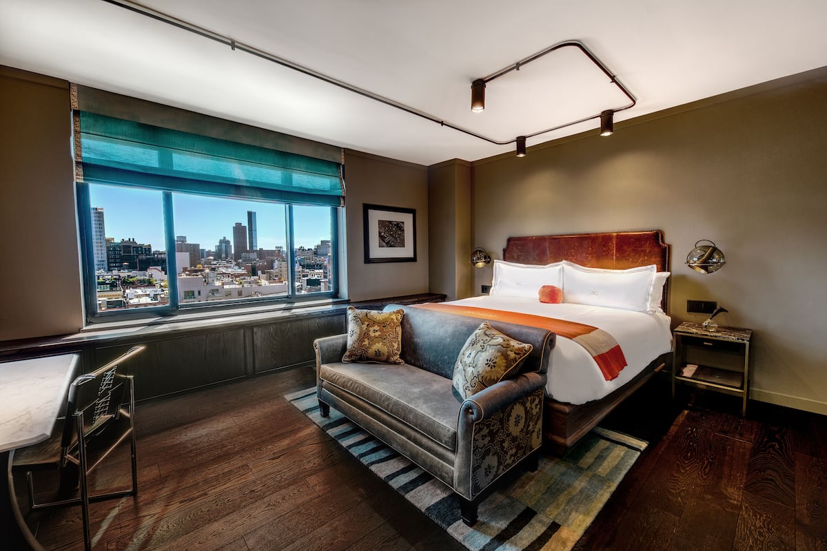 A hotel room with a large bed, a sofa, a desk, and a view of the city.