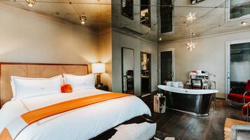 A modern hotel room with a large bed, a wooden headboard, a round breakfast bar, and a mirror.