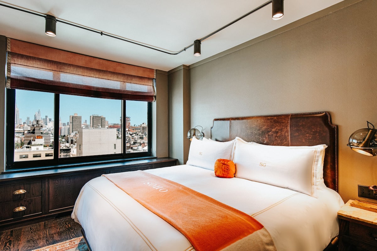 A hotel room with a large bed, a view of the city, and a city skyline visible through the window.