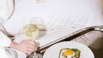 A person holding a glass of white wine, seated next to a plate with a dish containing an egg, avocado, and vegetables.