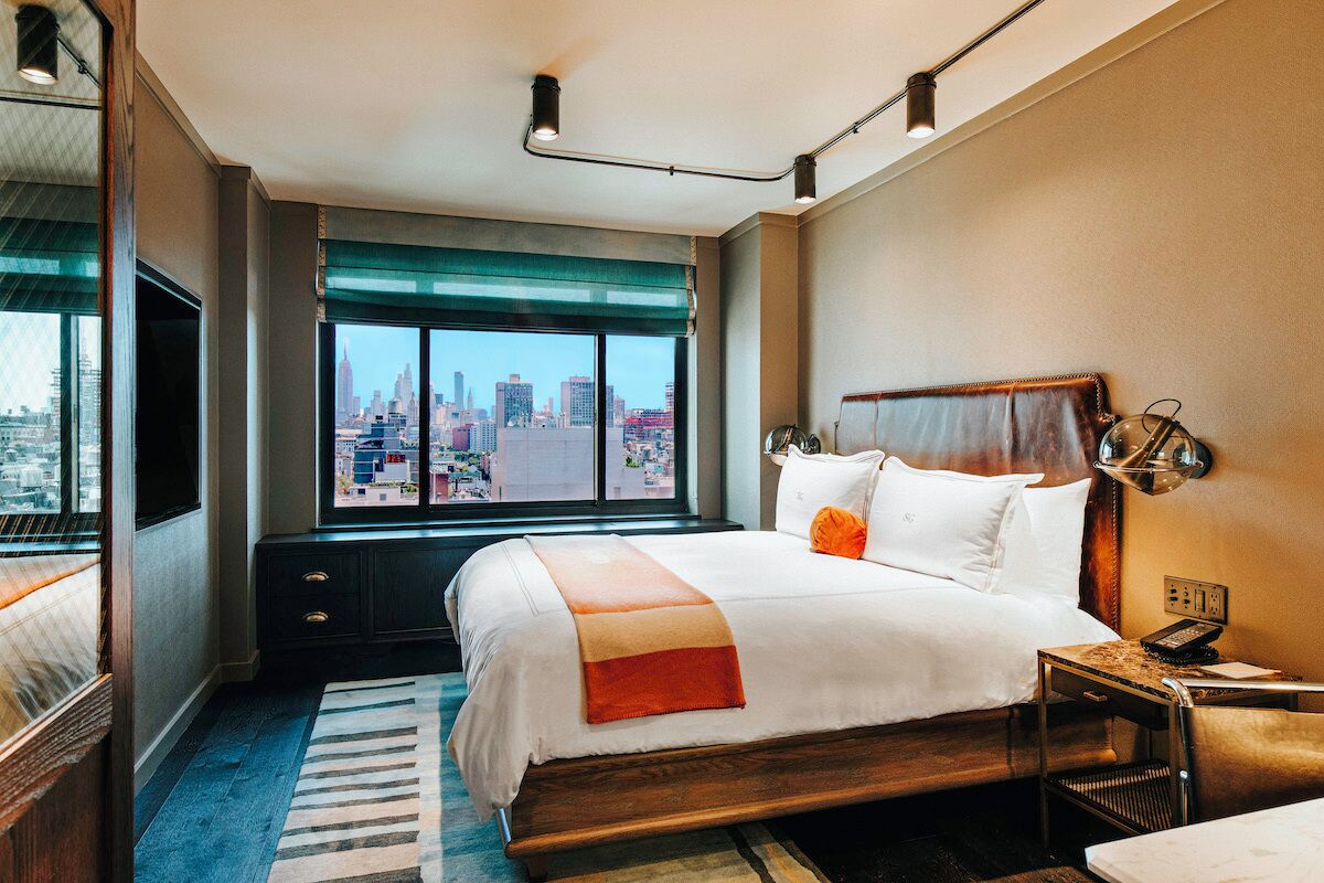 A hotel room with a large bed, a desk, a chair, a TV, and a window with a city view.
