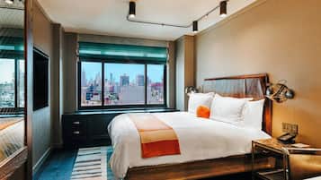 A hotel room with a large bed, a desk, a chair, a TV, and a window with a city view.
