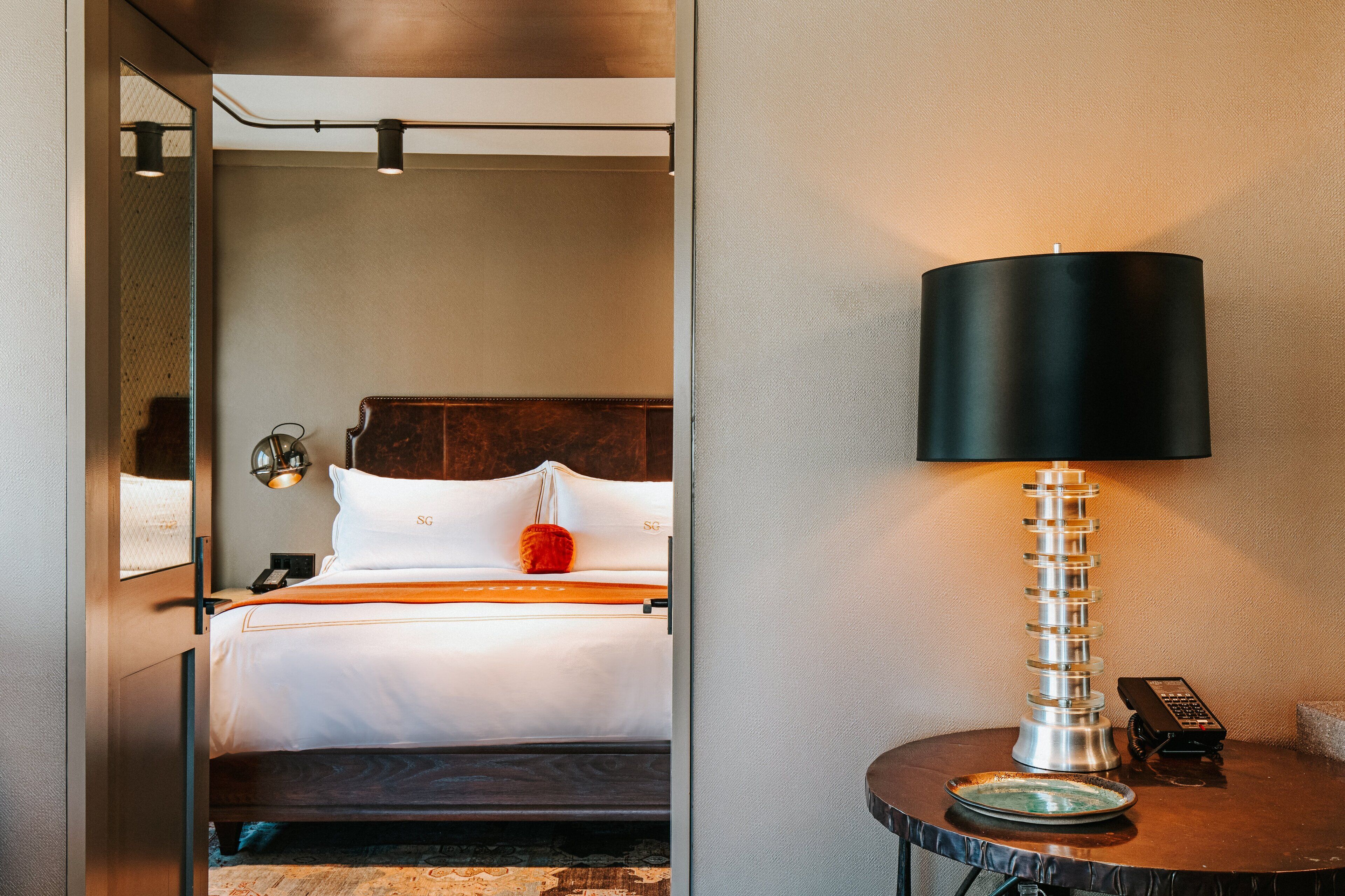 A hotel room with a bed, a round table with a lamp, and a telephone.