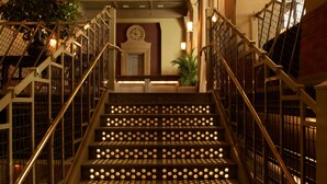 Eine Treppe mit runden Lichtern auf jedem Tritt, gesäumt von Metallgeländern, die zu einem Zwischenpodest mit einer Uhr und einer Tür führt.
