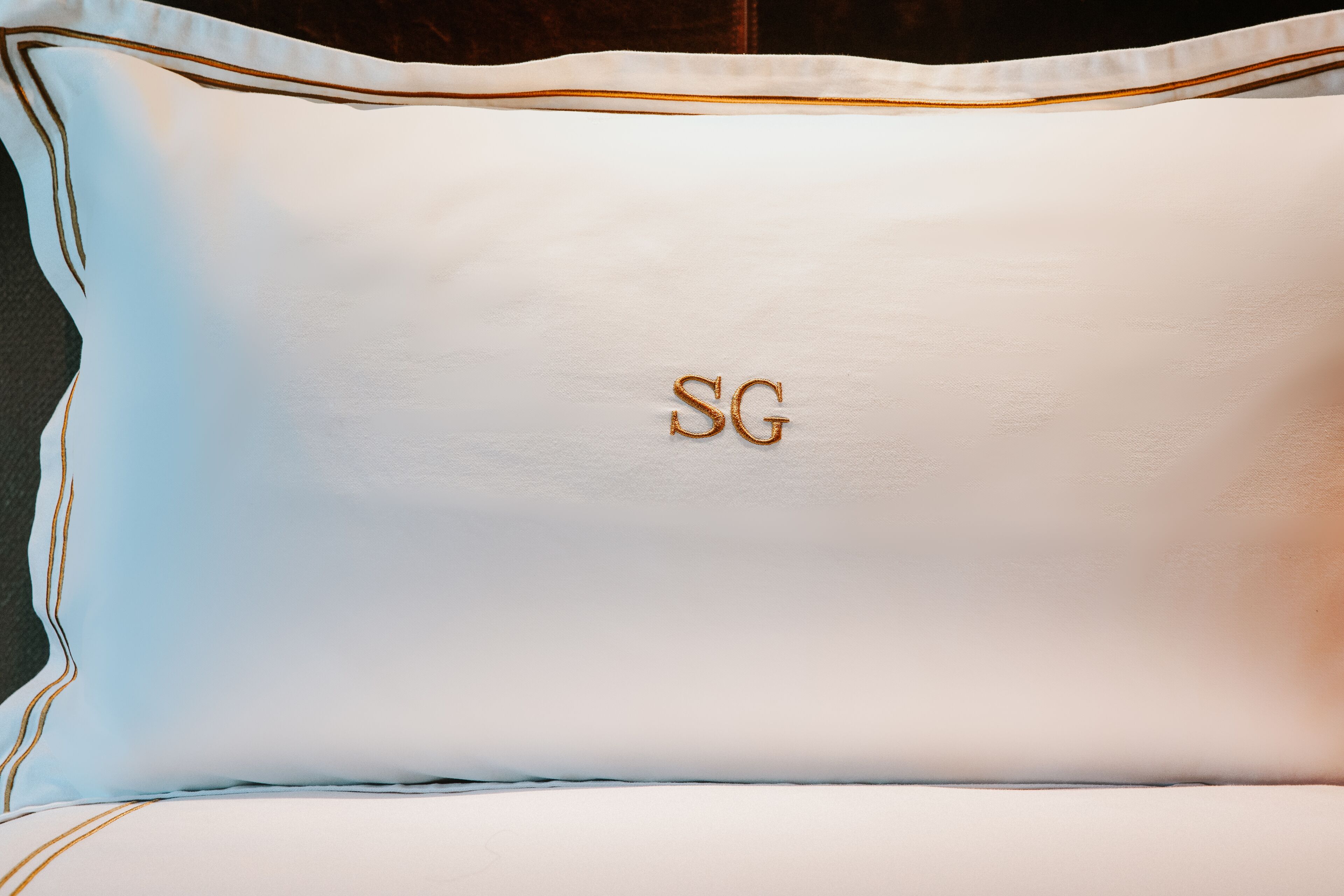 A pillow with embroidered initials "SG" on a white and light blue fabric.