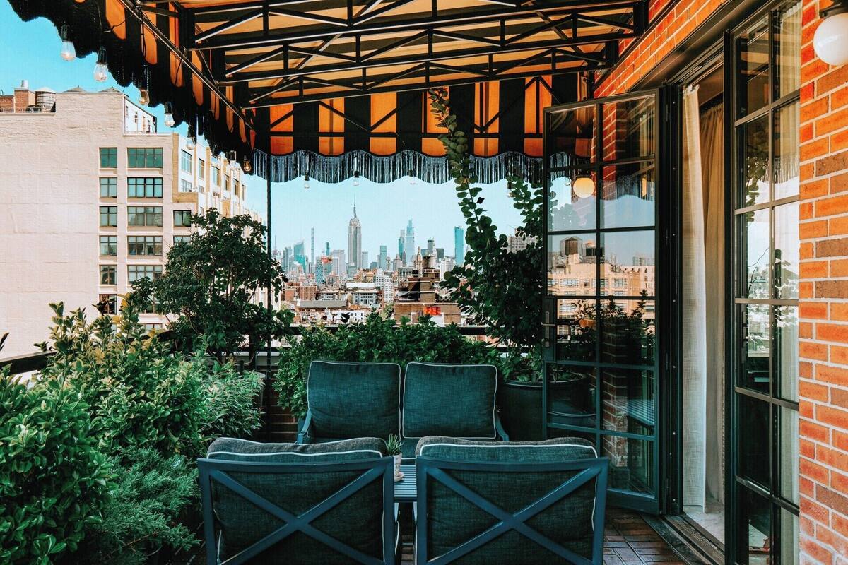 An outdoor seating area with chairs and tables, a city skyline view, and a brick building facade.